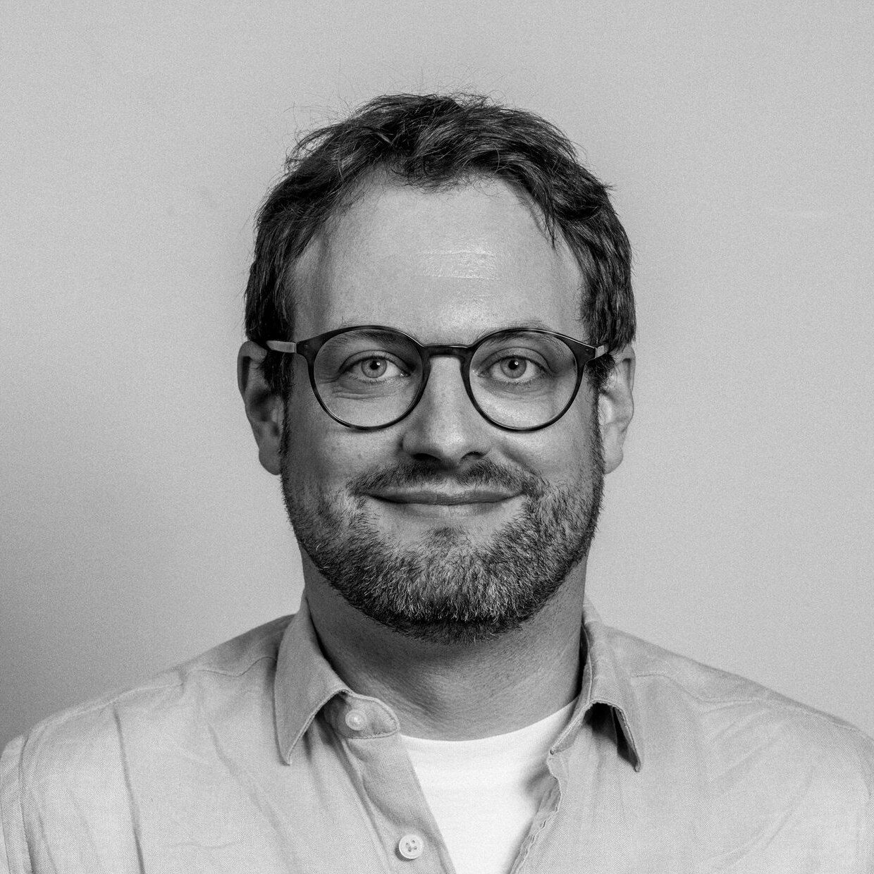 David Kobelt vor hellgrauem Hintergrund, Schwarzweiss-Porträt.